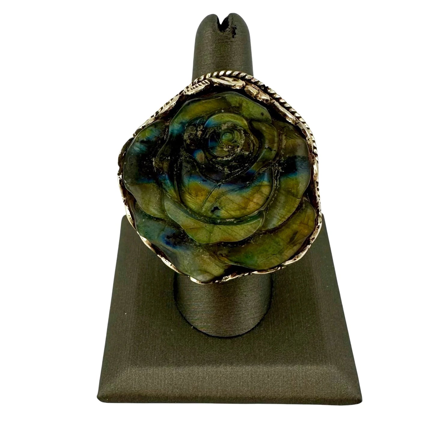 Rose-shaped ring with green and gold design on a gray stand against a white background