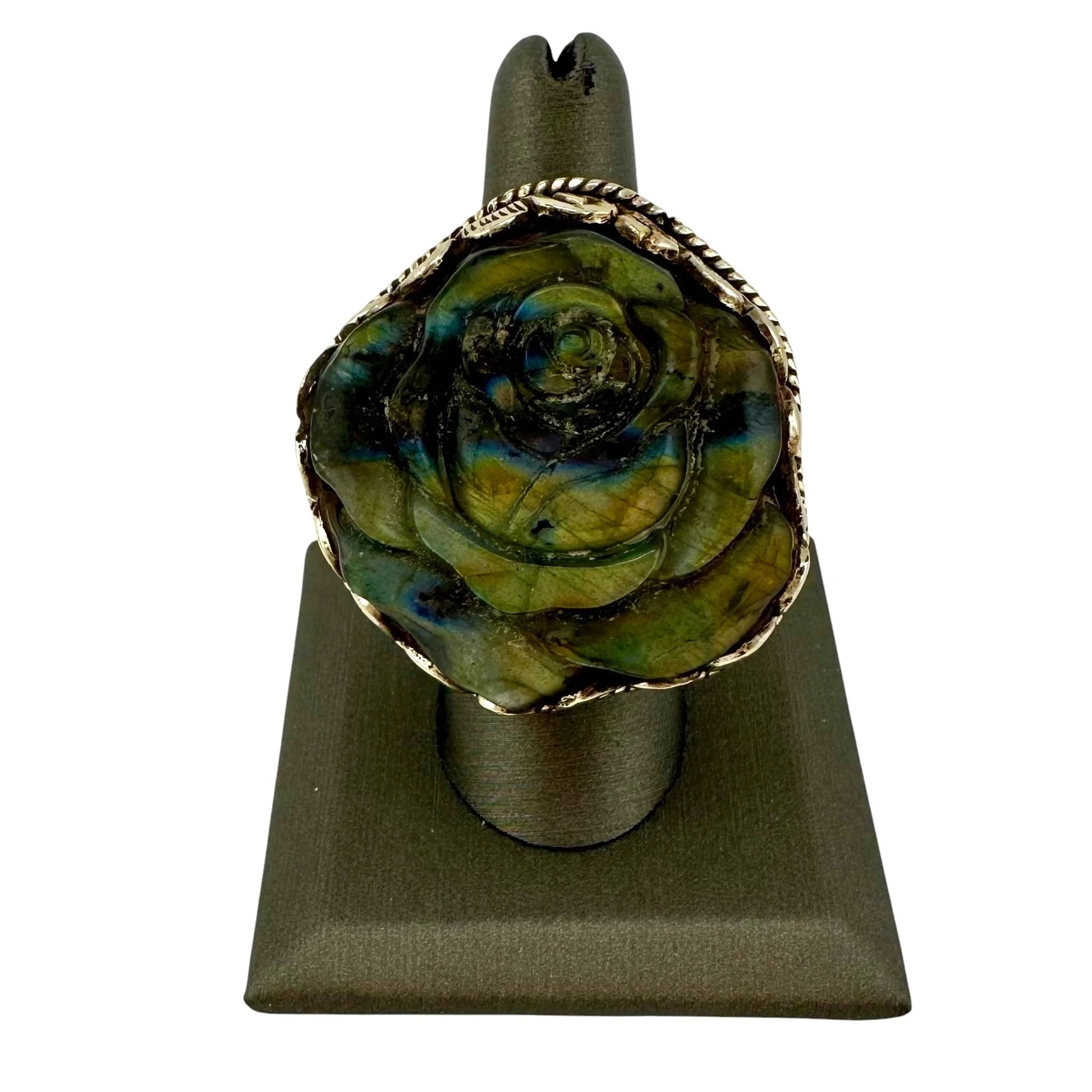 Rose-shaped ring with green and gold design on a gray stand against a white background