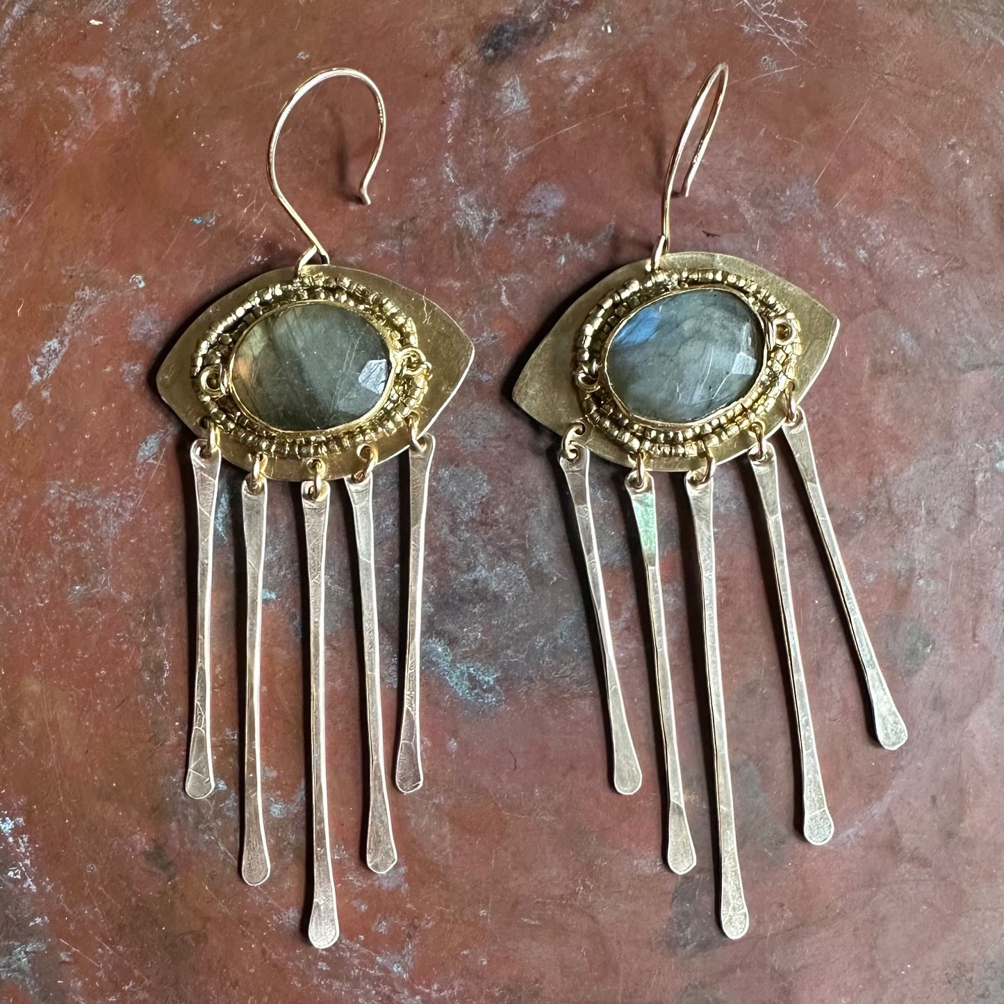 Gold and silver earrings with gemstone center on a textured brown surface