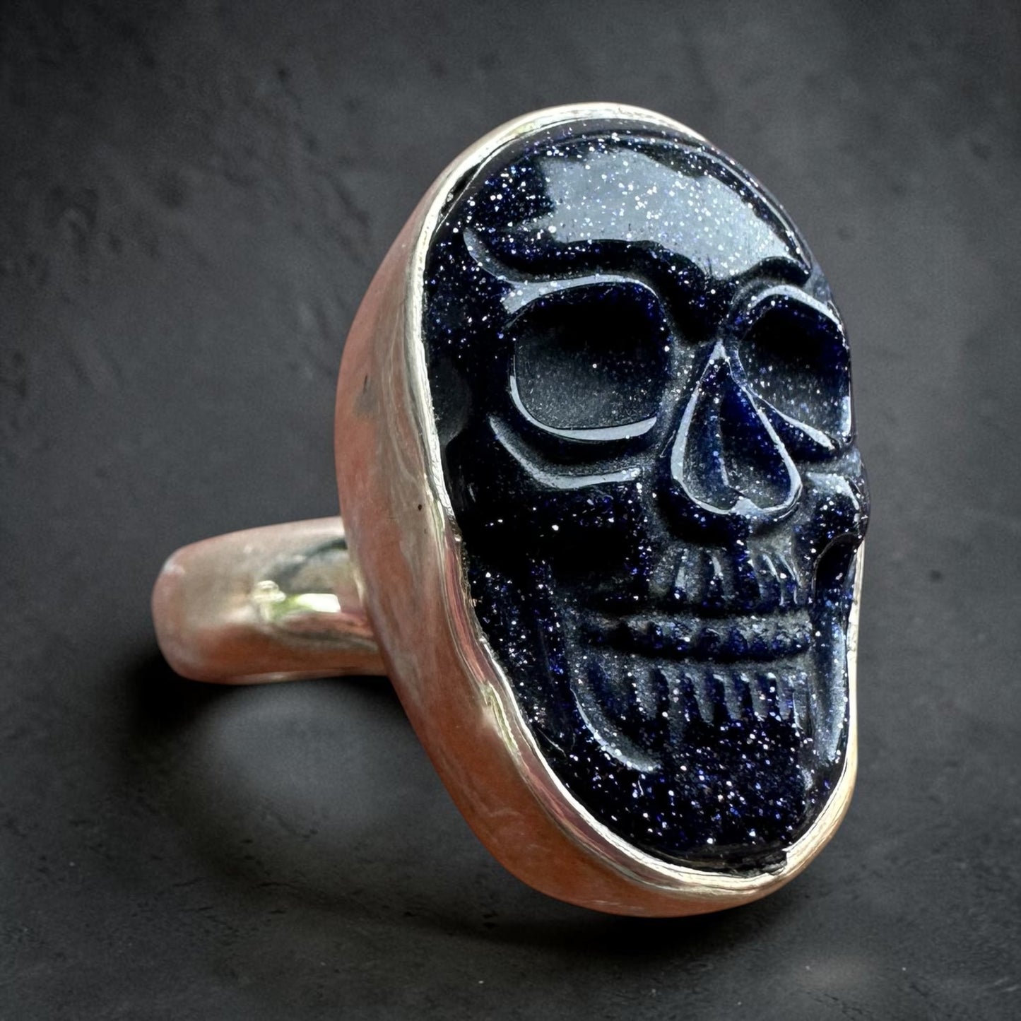 Skull-shaped sterling silver ring with dark indigo stone on a dark background