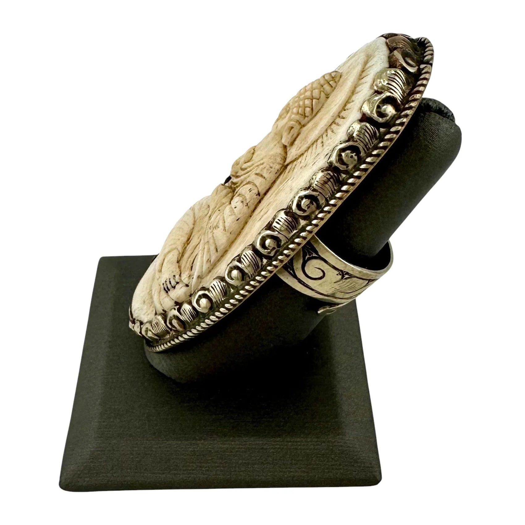 Side view of a carved bone seated Buddha figure in a meditative pose on a large silver ring on a white background