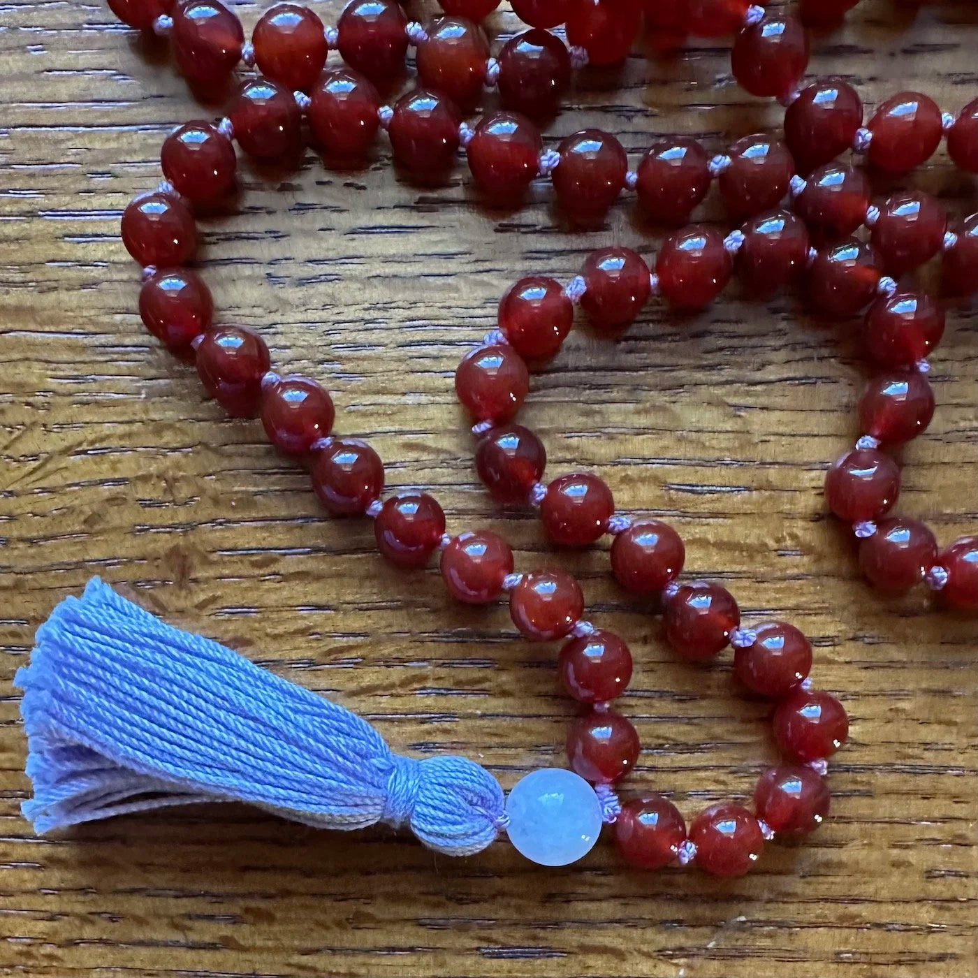 Red carnelian beaded necklace with a lavender guru bead and tassel on a wooden surface