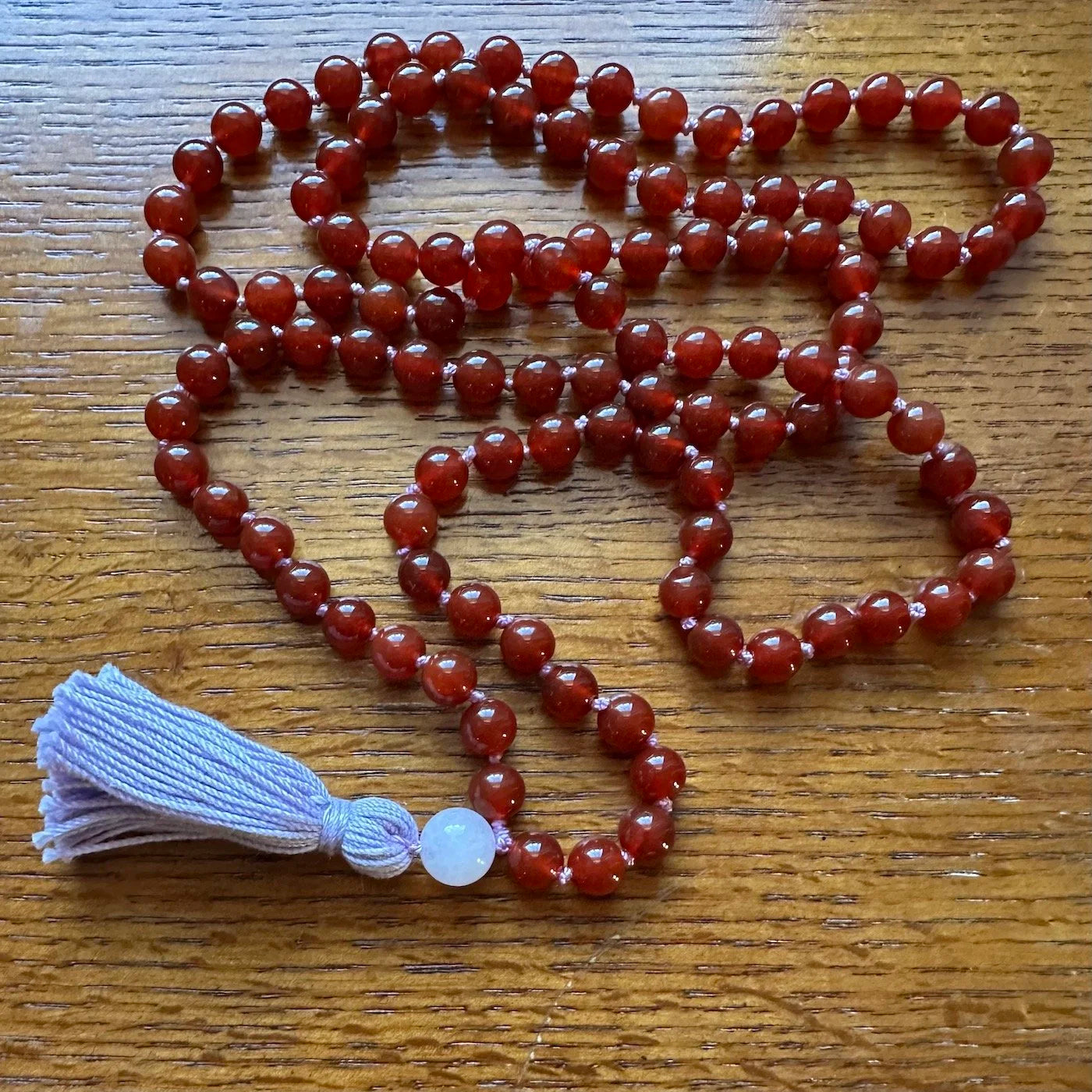 Red beaded necklace with a tassel on a wooden surface