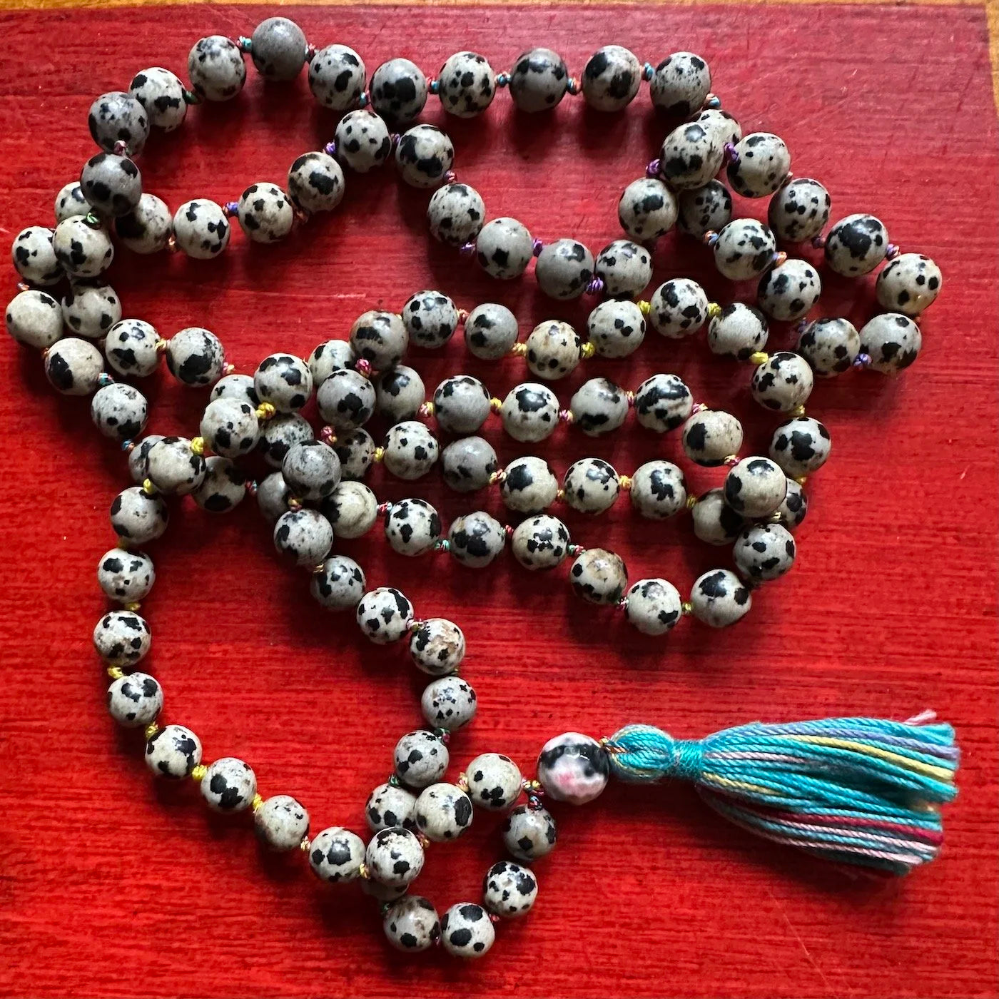 Mala necklace with black and white beads and a colorful rainbow tassel on a red surface
