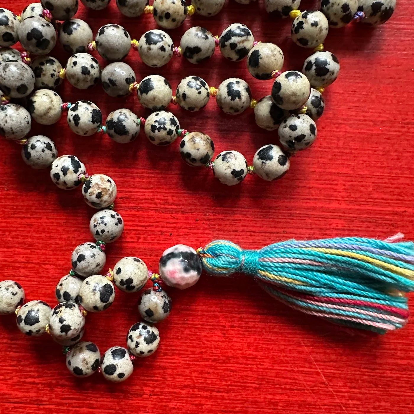 String of spotted Dalmatian jasper beads with a colorful tassel on a red surface