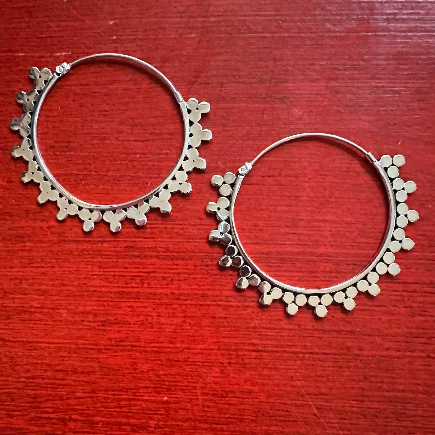 Silver Indonesian tribal hoop earrings with floral patterns on a red wooden surface