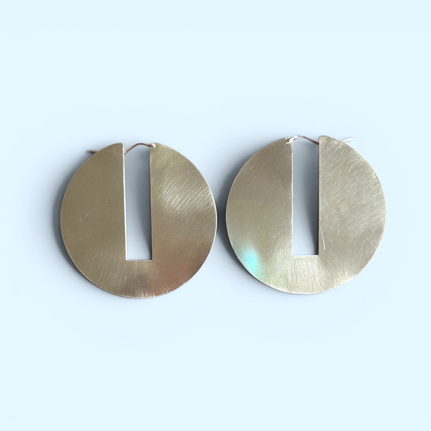 Pair of geometric brass hoop earrings on a light blue background