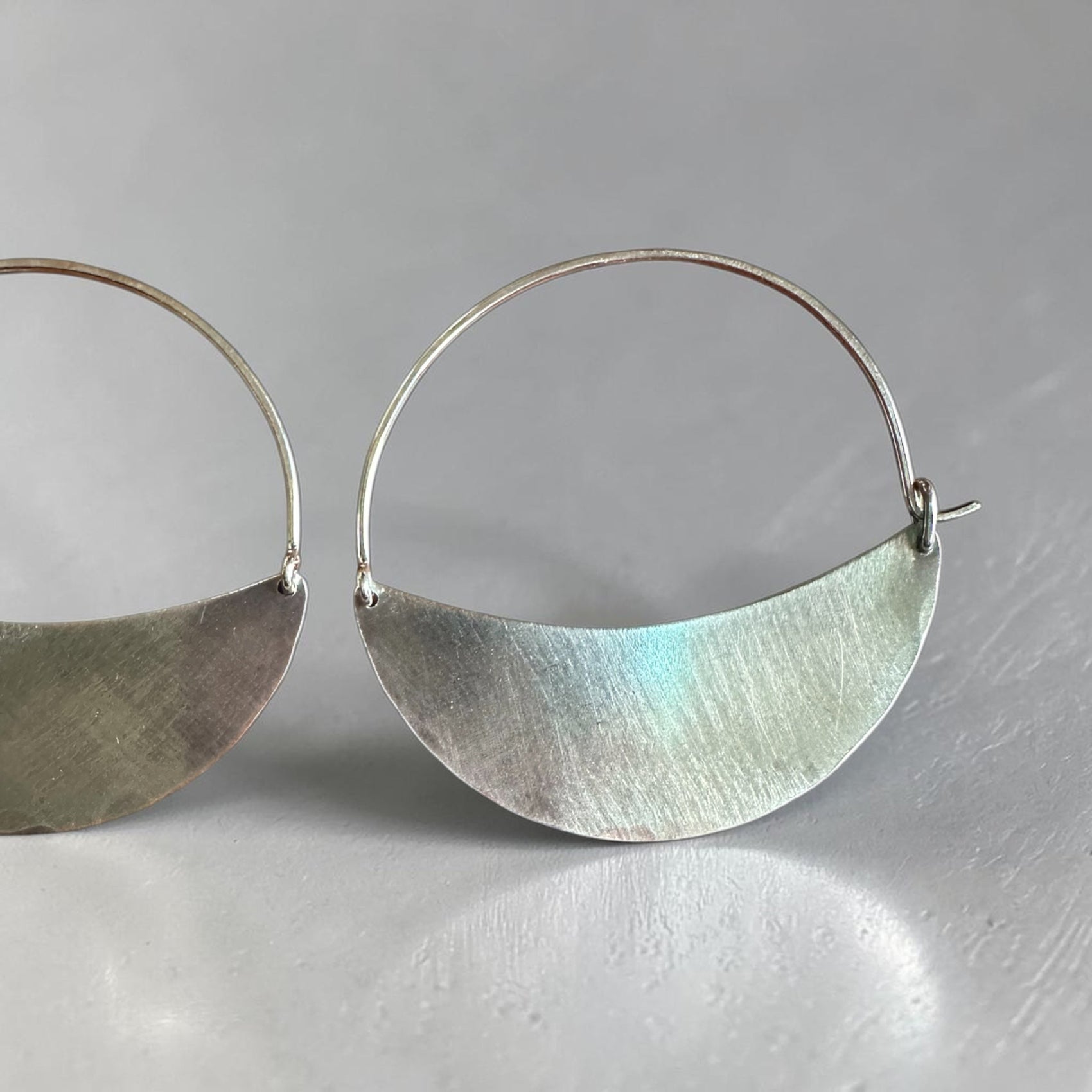 Silver hoop earrings with half-circle pendants on a gray background