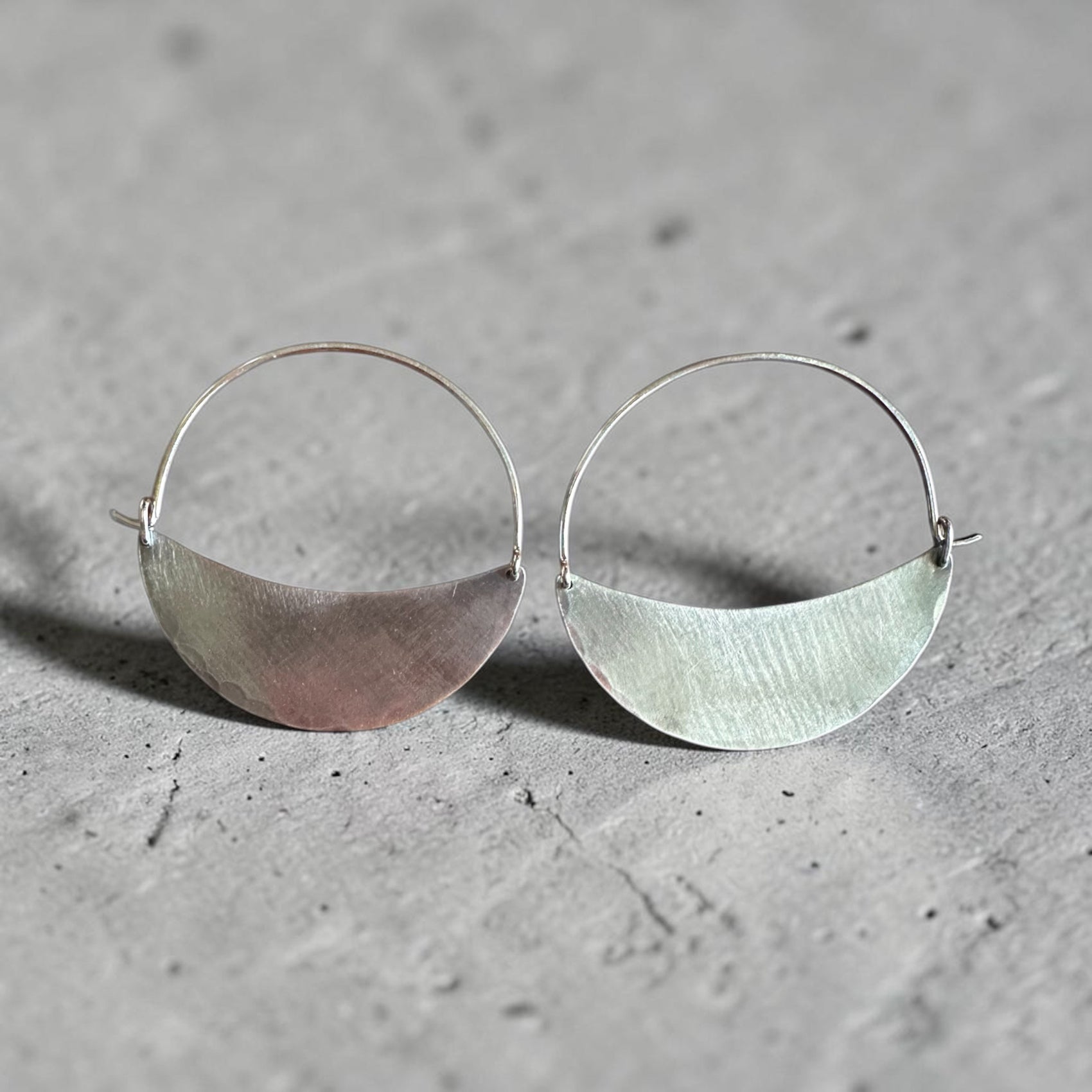 Silver hoop earrings with half-circle design on a gray surface