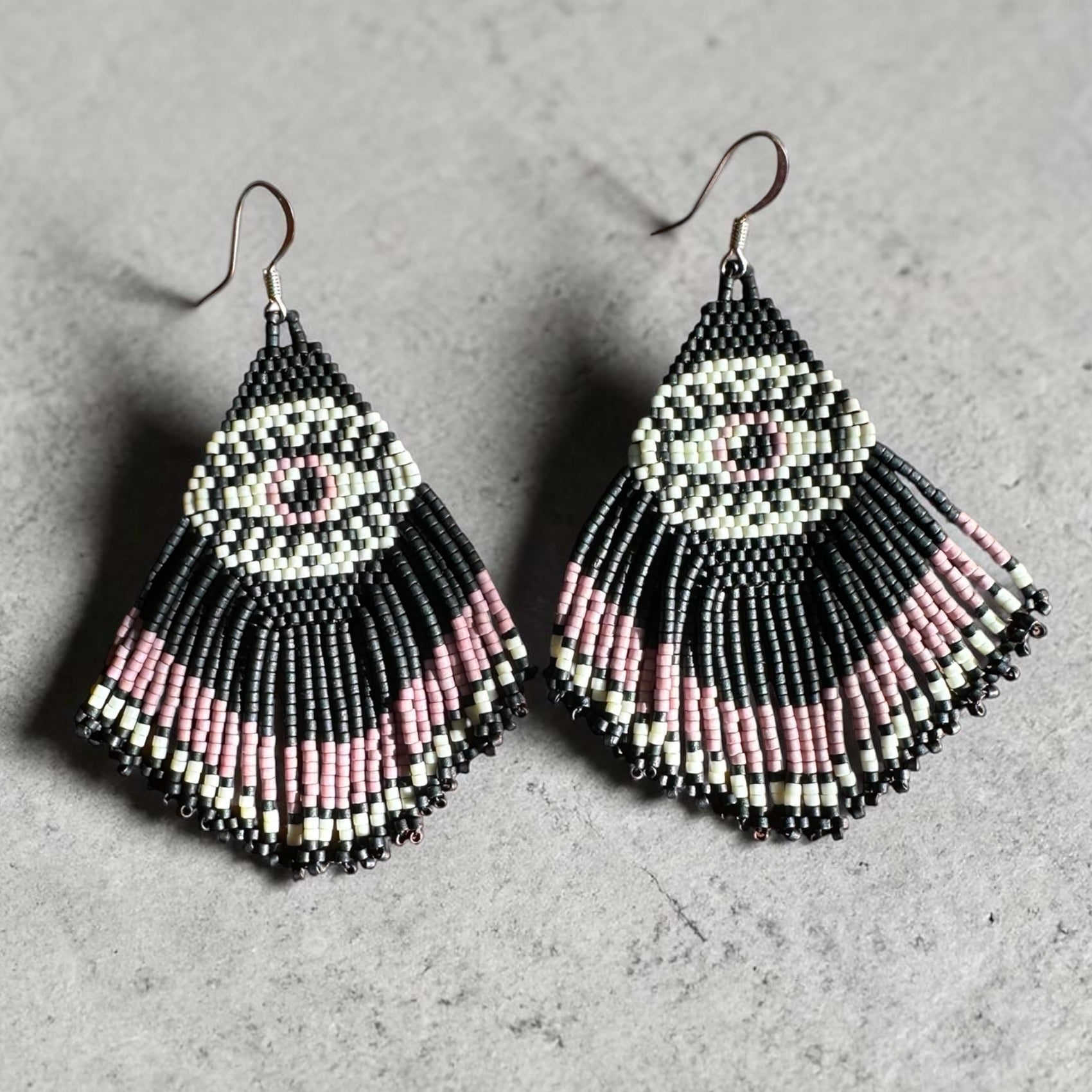 Pair of beaded earrings with black, pink, and white mystic eye pattern on a gray background