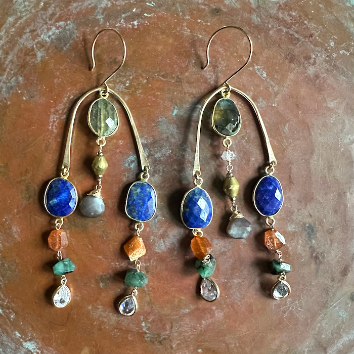 Pair of chandelier brass earrings with colorful gemstones on a textured brown surface 