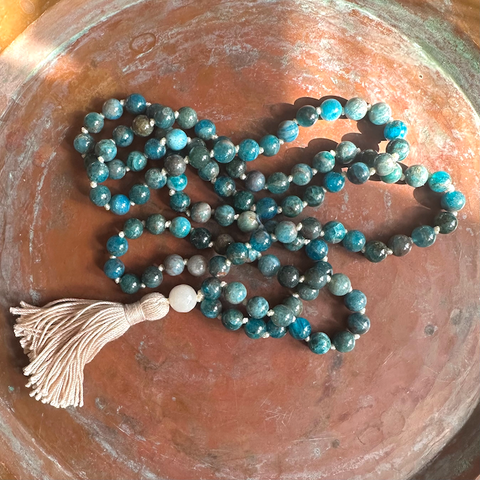 Beaded apatite mala with a white tassel on a textured surface