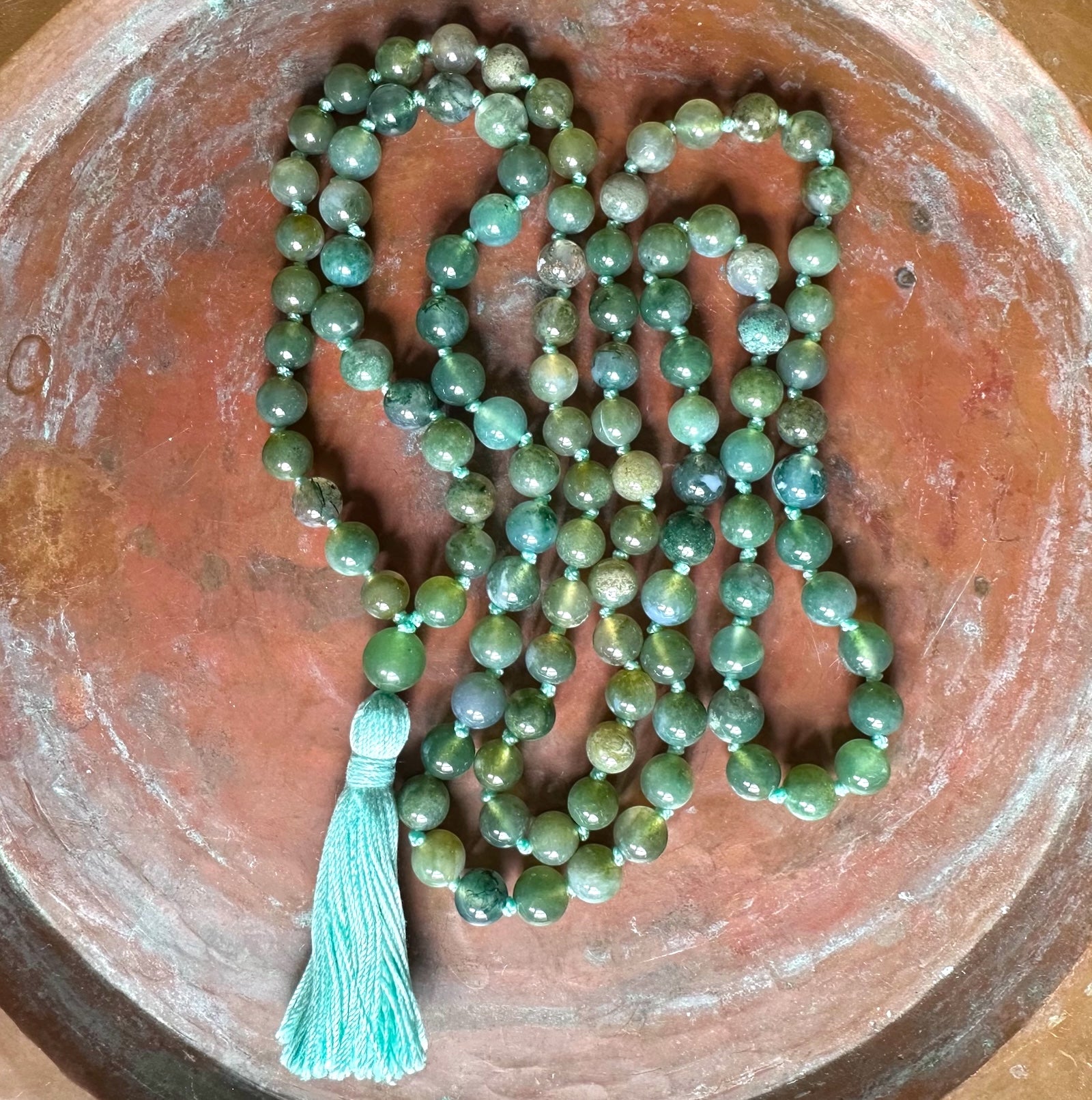 Green beaded necklace with a tassel on a rustic wooden surface