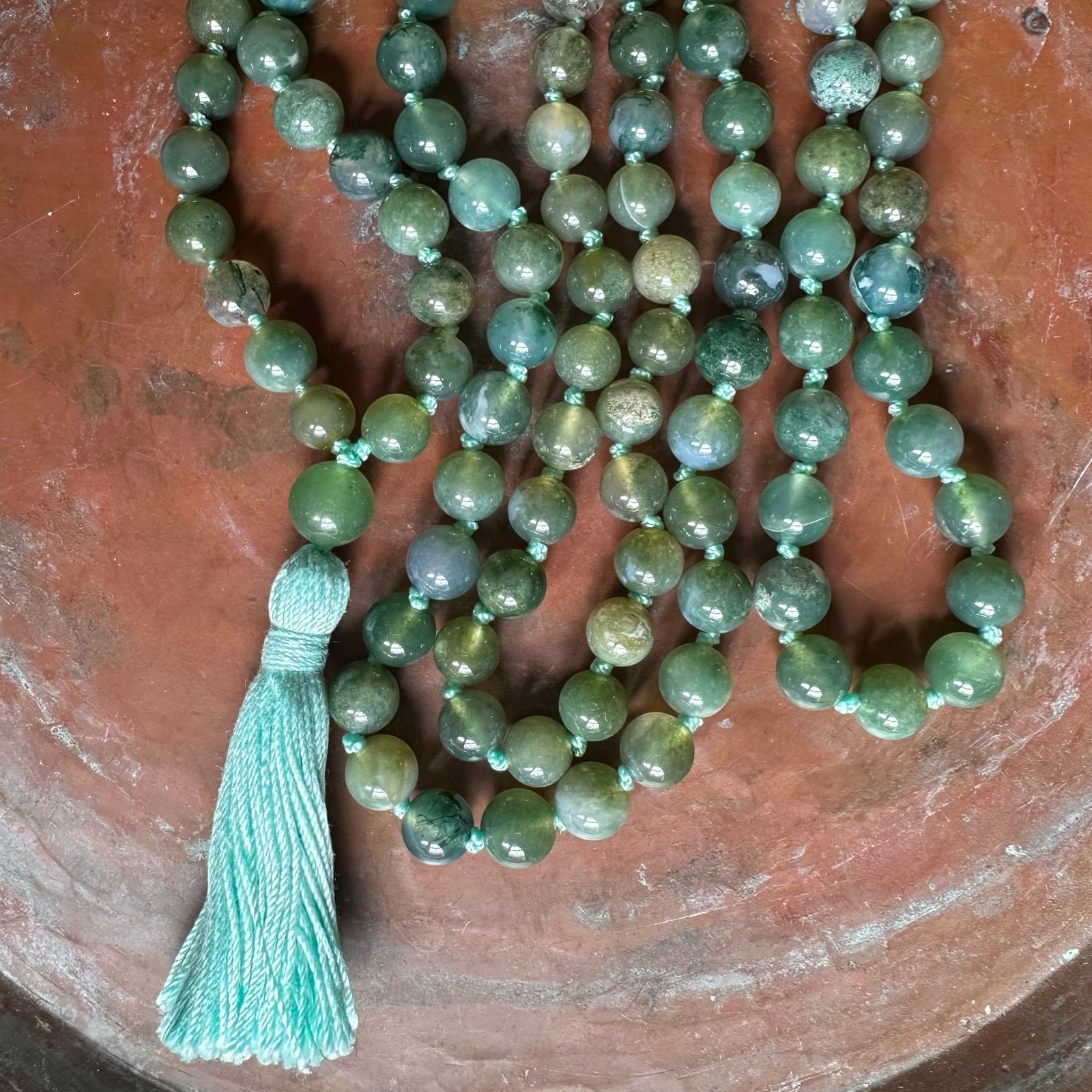 Green beaded necklace with a tassel on a brown surface