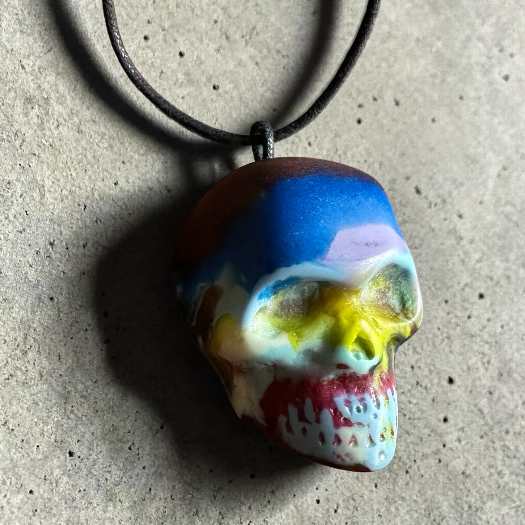 Colorful skull-shaped pendant on a necklace against a textured surface