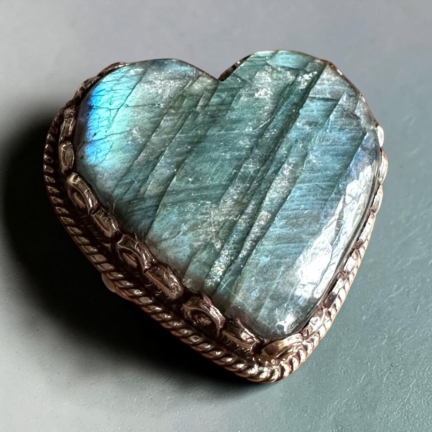 Heart-shaped labradorite stone with a decorative metal frame on a gray background