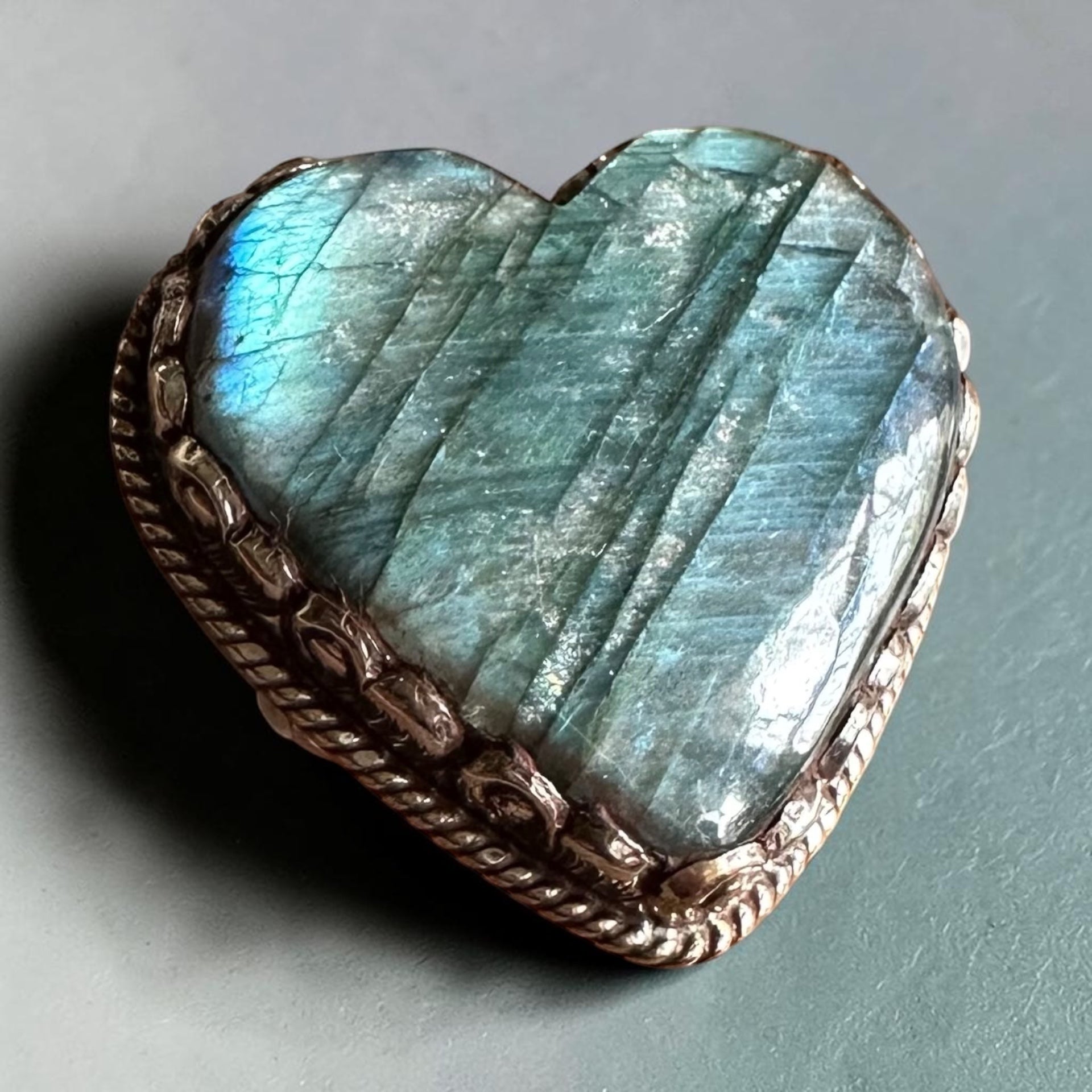 Heart-shaped labradorite stone with a decorative metal frame on a gray background