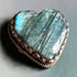 Heart-shaped labradorite stone with a decorative metal frame on a gray background