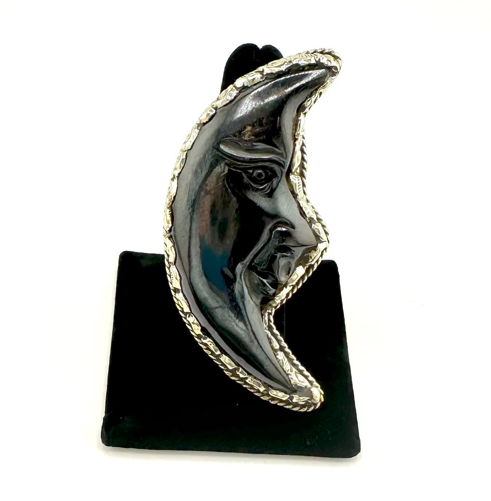 Black and silver crescent moon-shaped ring on a black stand against a white background