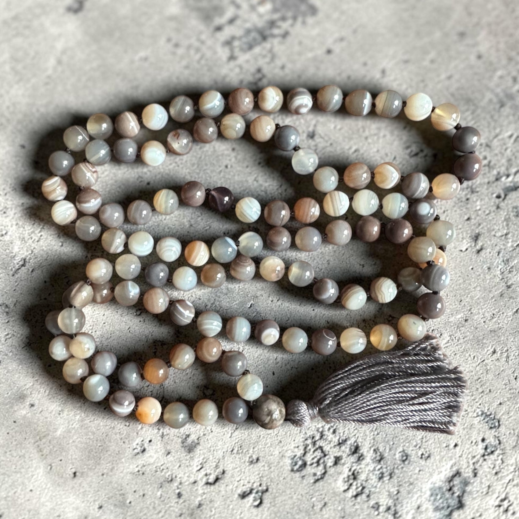 String of Botswana agate beads with a tassel on a textured surface