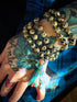 Hand holding a beaded Dalmatian Jasper mala with a colorful tassel against a tattooed arm.