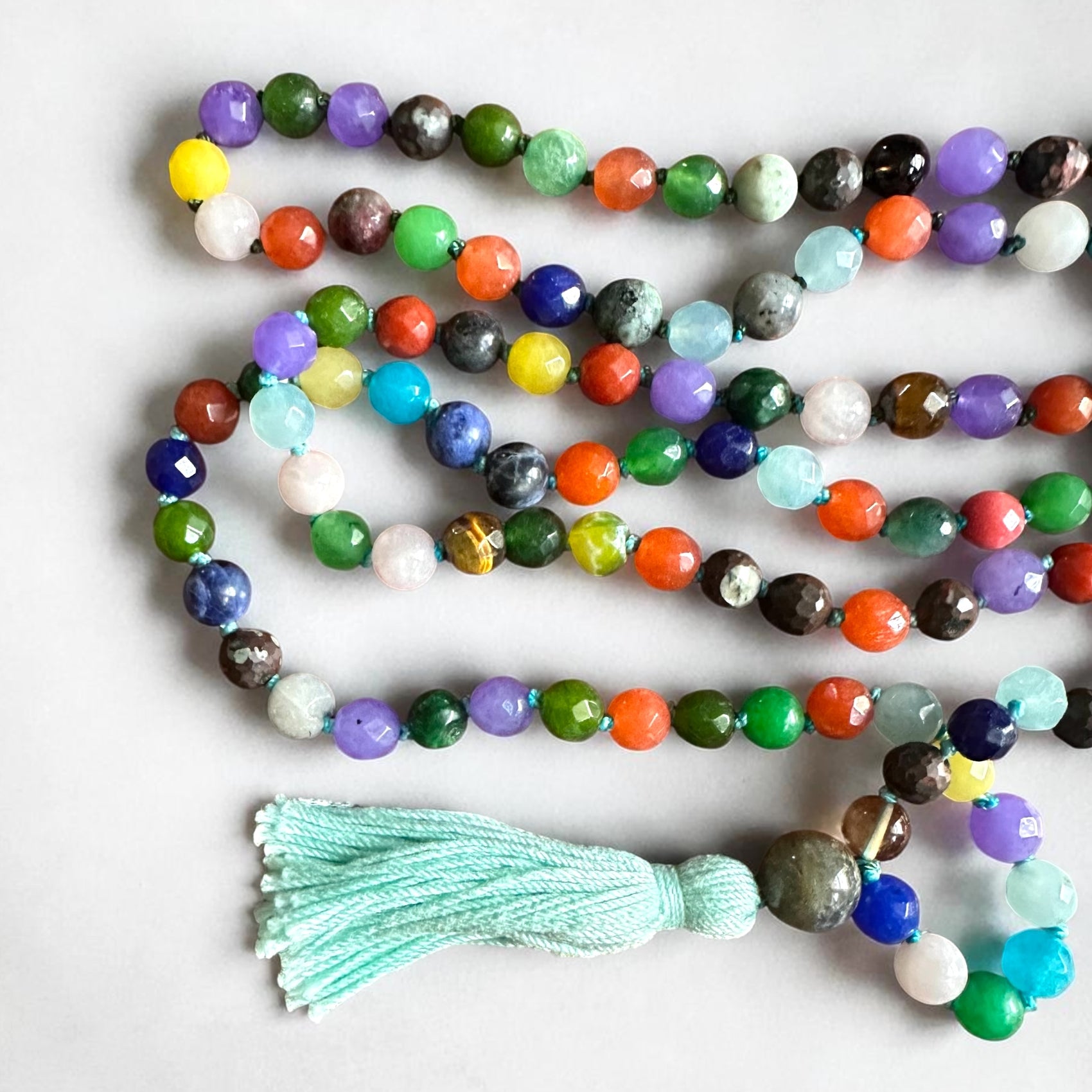 Close up of colorful beaded agate mala necklace with aqua tassel on a white background