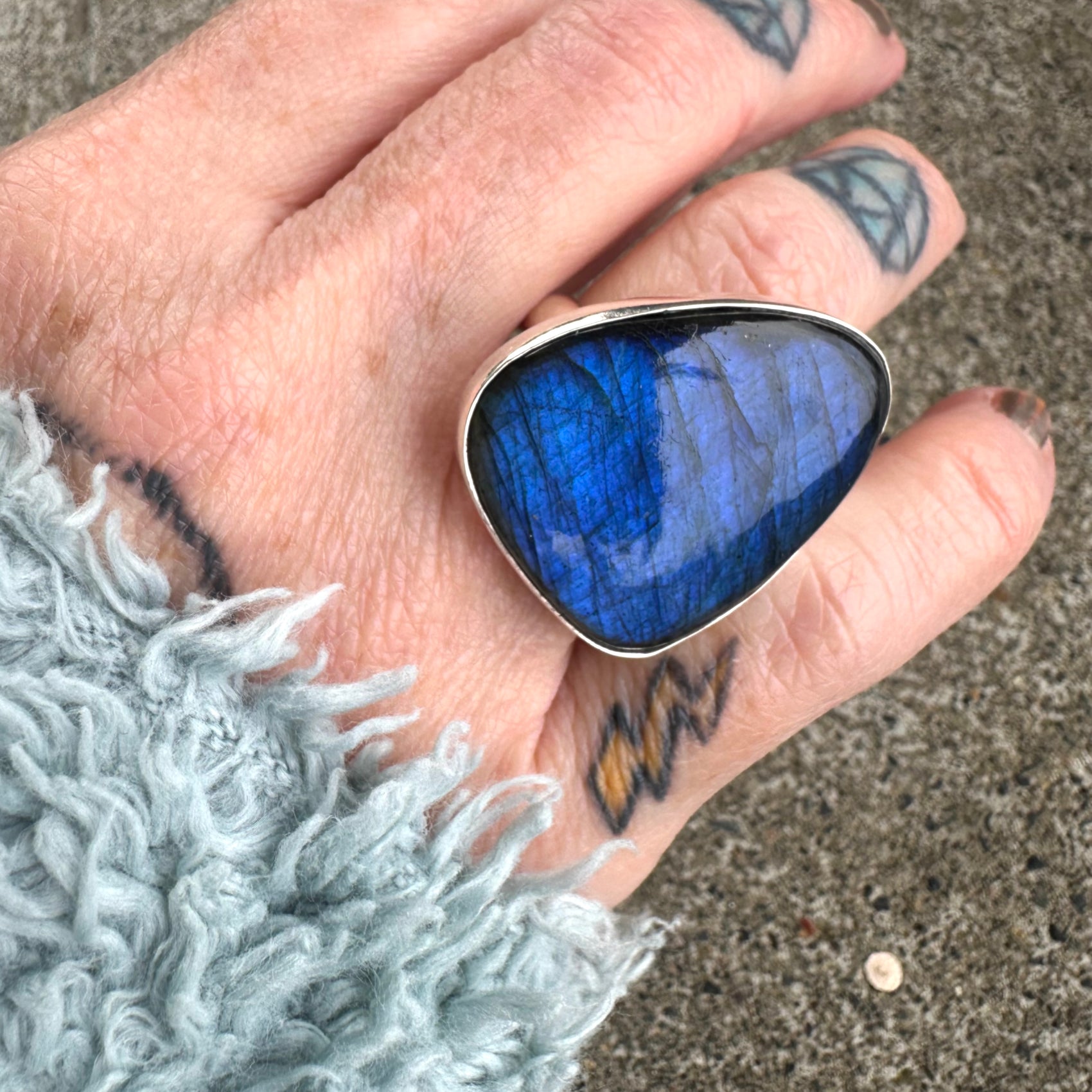 Hand wearing a blue stone ring with a textured gray sleeve.