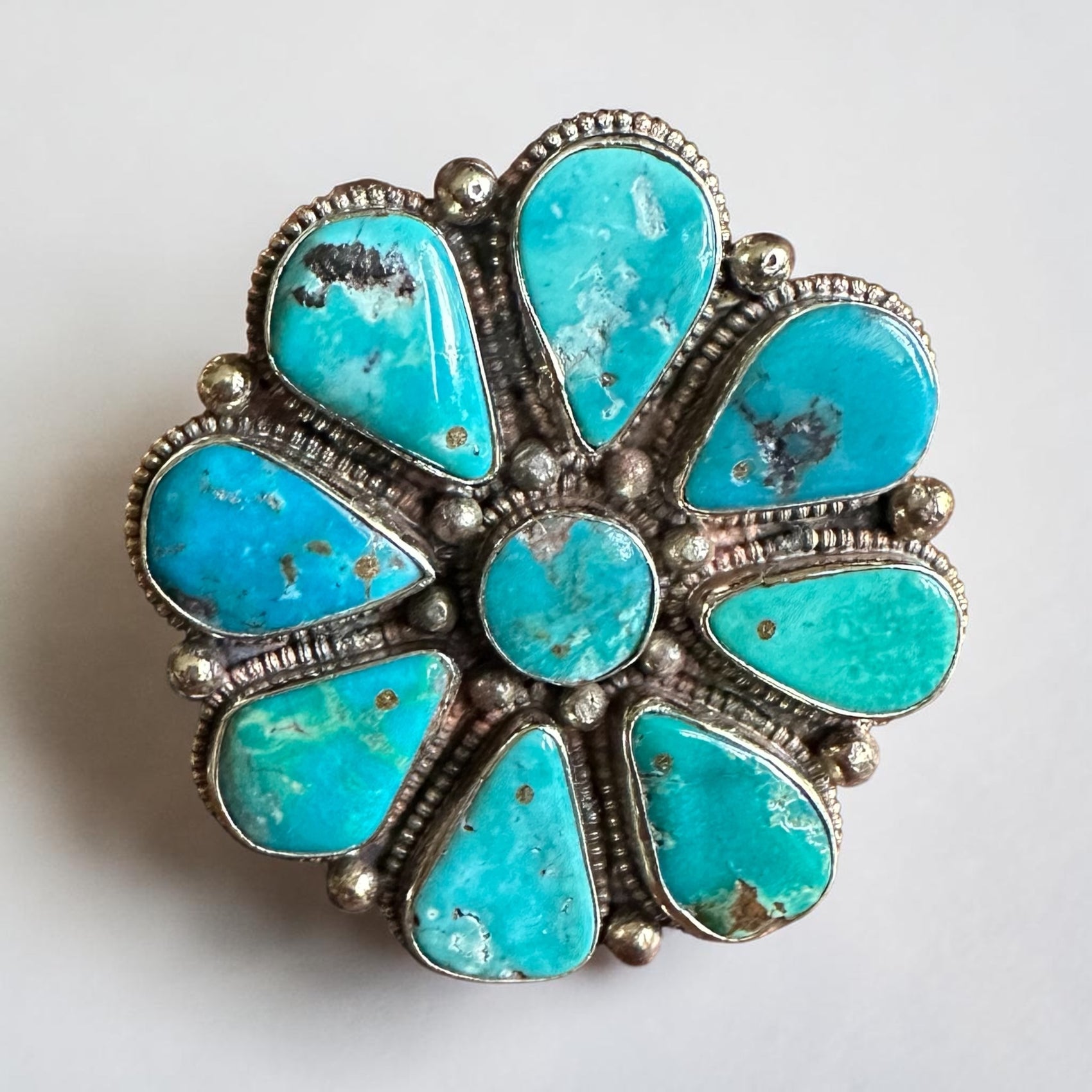 Turquoise stone floral ring with silver setting on a light gray background