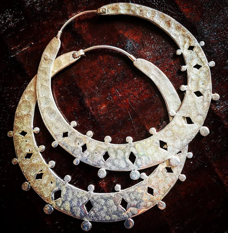 Pair of three inch Indonesian hand made silver hoop earrings on a dark wooden surface