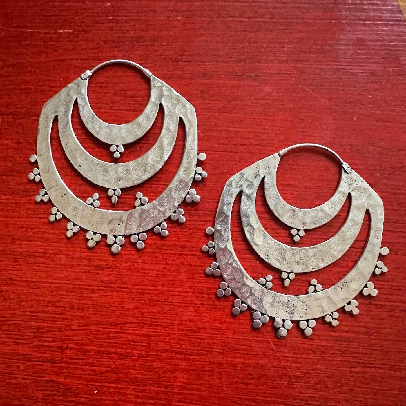 Pair of Indonesian tribal silver hoop earrings with small spherical accents on a red wooden surface